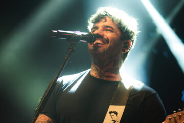 Lucas Silveira, vocalista da Fresno, em apresentação ao vivo com guitarra e iluminação dramática no palco