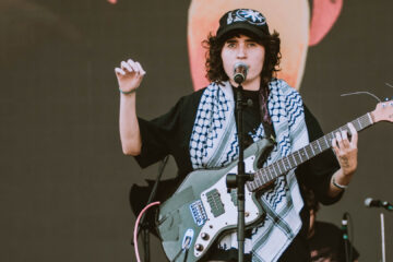 Sophia Chablau no Lollapalooza 2025 com keffiyeh palestino e guitarra, durante performance com protesto político.