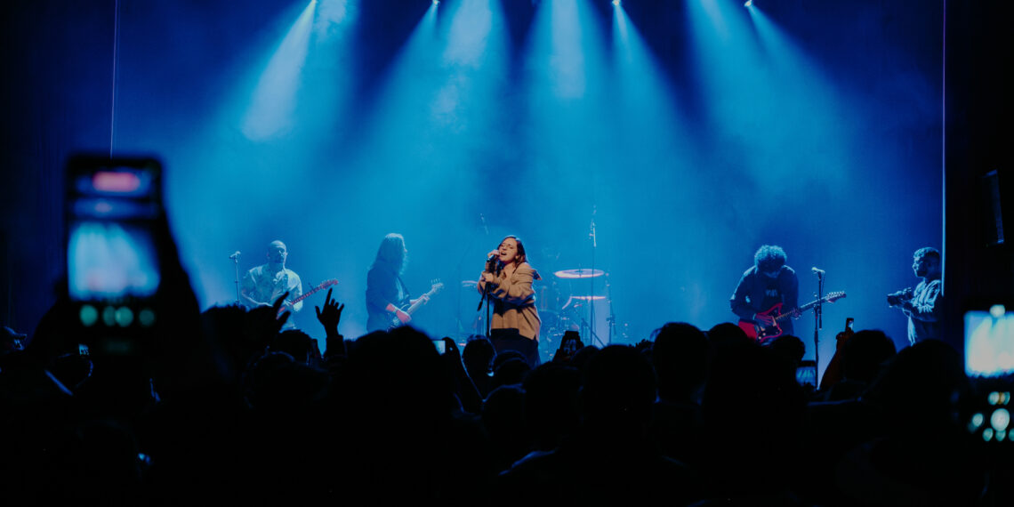 Banda Adorável Clichê se apresenta com luzes azuis intensas para um público atento na Casa Natura Musical em São Paulo, em show marcante de shoegaze.