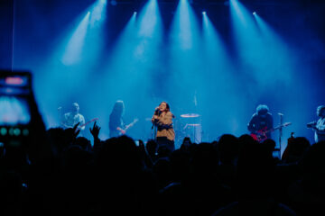 Banda Adorável Clichê se apresenta com luzes azuis intensas para um público atento na Casa Natura Musical em São Paulo, em show marcante de shoegaze.