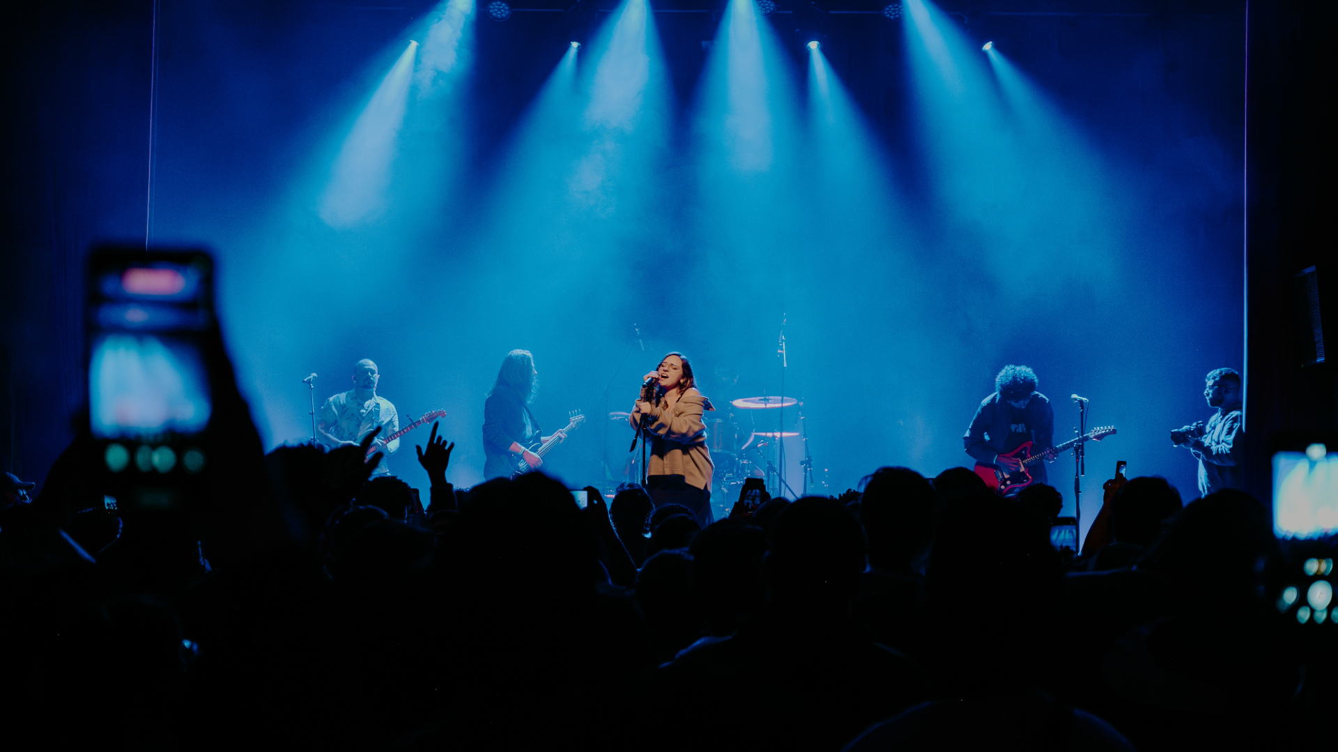Banda Adorável Clichê se apresenta com luzes azuis intensas para um público atento na Casa Natura Musical em São Paulo, em show marcante de shoegaze.