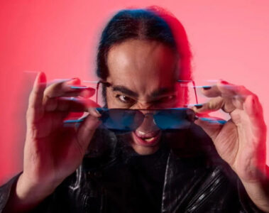 Daron Malakian, guitarrista do System of a Down e líder do Scars on Broadway, em ensaio promocional do álbum Addicted to the Violence, usando óculos escuros e jaqueta de couro, com fundo vermelho estilizado