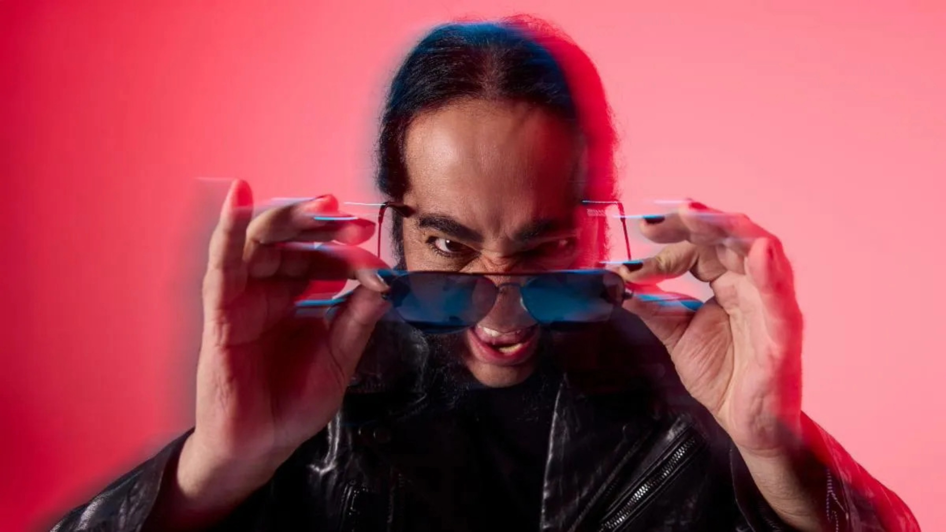 Daron Malakian, guitarrista do System of a Down e líder do Scars on Broadway, em ensaio promocional do álbum Addicted to the Violence, usando óculos escuros e jaqueta de couro, com fundo vermelho estilizado