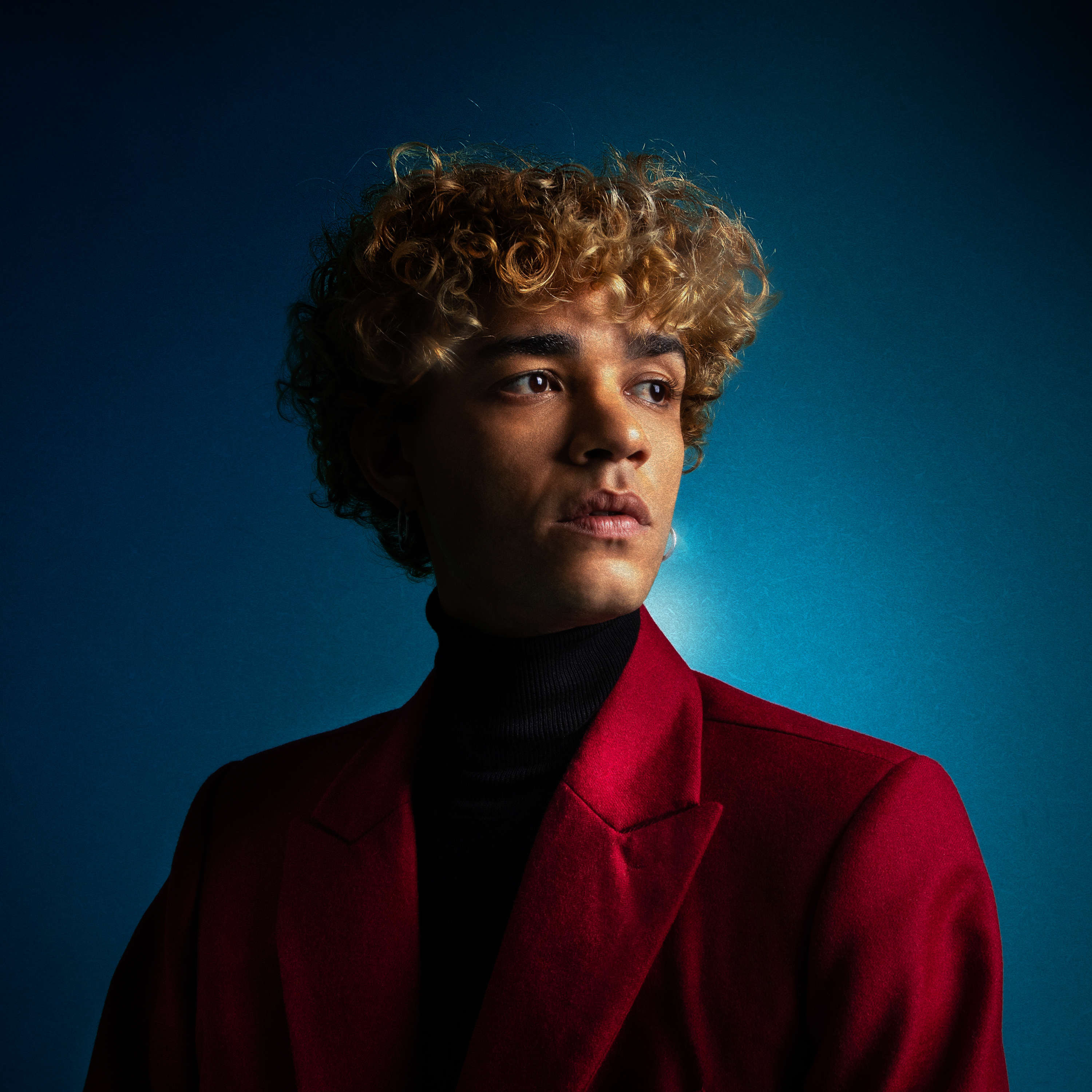 Retrato do cantor Do Prado com fundo azul, usando blazer vermelho. Divulgação do álbum Quantas vezes é possível se apaixonar?