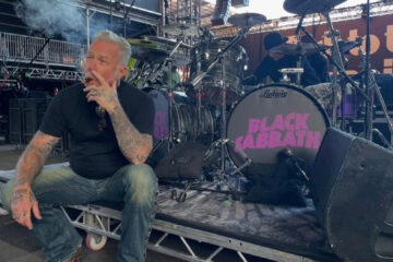 James Hetfield sentado no backstage, fumando charuto em frente à bateria com logo do Black Sabbath antes do show “Back to the Beginning”.