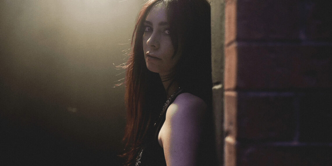 LØLØ posa em ambiente sombrio com iluminação suave, promovendo o single the devil wears converse