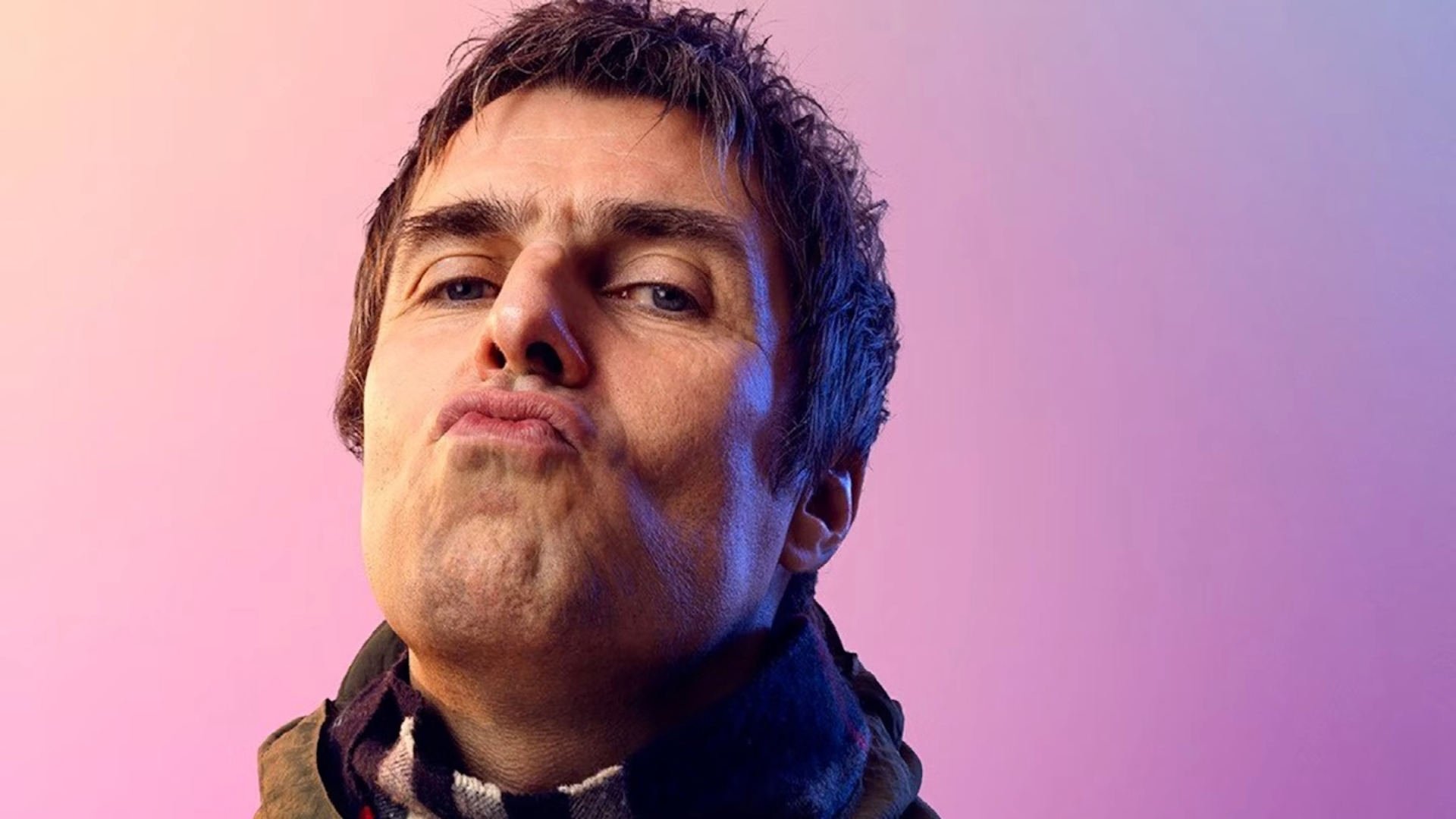 Retrato de Liam Gallagher encarando a câmera com expressão desafiadora, sobre fundo rosa e roxo.
