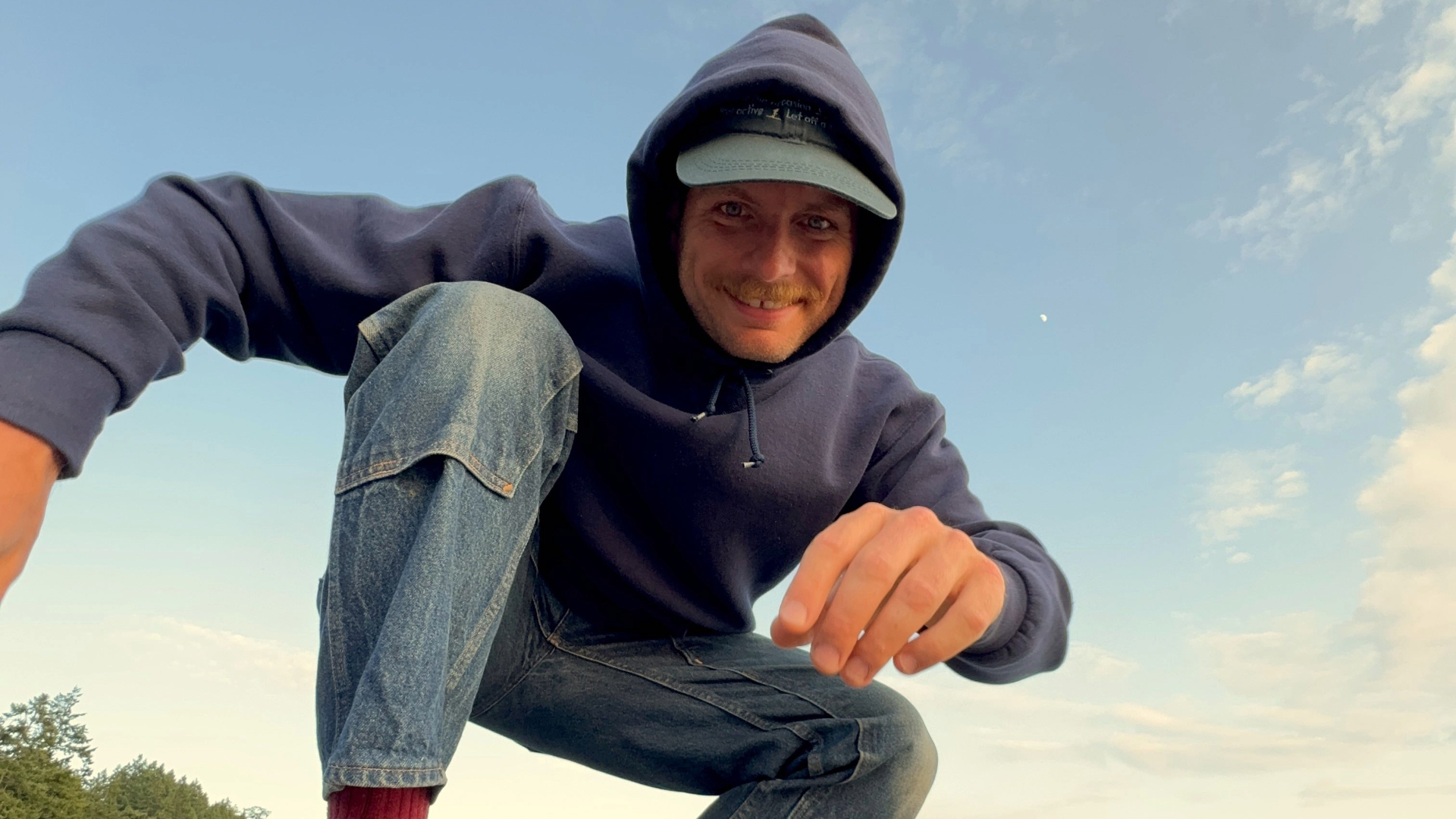 Mac DeMarco agachado em rocha à beira-mar, sorrindo, em clima informal — imagem usada na divulgação do show no Brasil em 2026