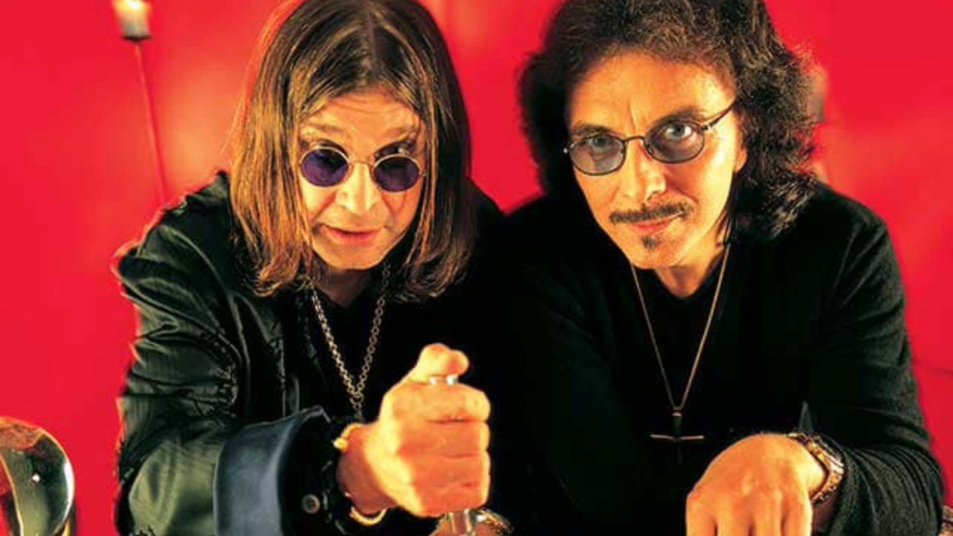 Ozzy Osbourne e Tony Iommi juntos em imagem promocional com fundo vermelho, representando a irmandade do Black Sabbath.