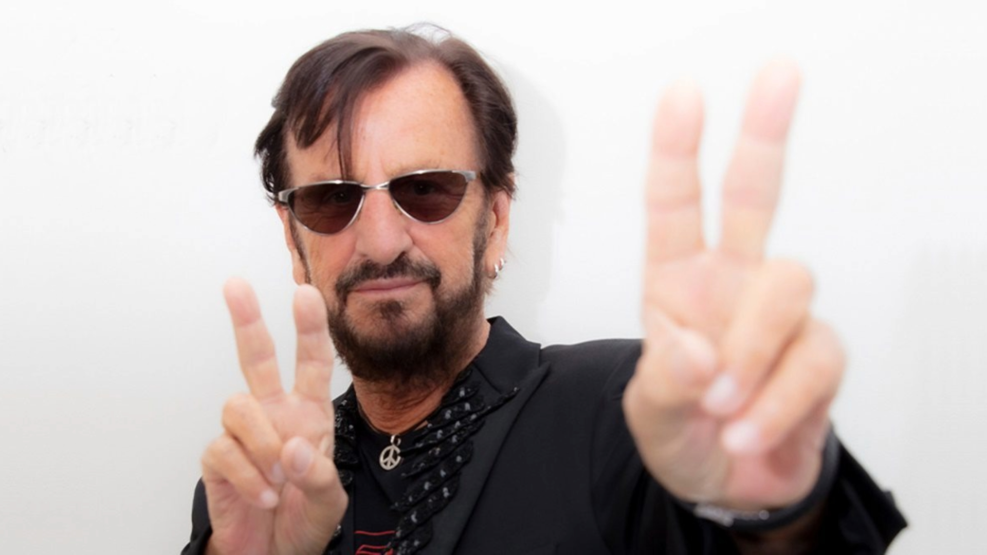Ringo Starr durante apresentação ao vivo, segurando baquetas, com luz vermelha ao fundo