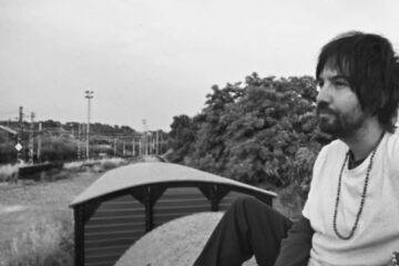 Kevin Parker sentado em um vagão de trem em imagem promocional do single End of Summer do Tame Impala