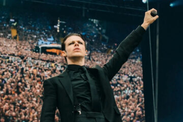 Yungblud com microfone erguido diante de uma multidão durante show ao ar livre