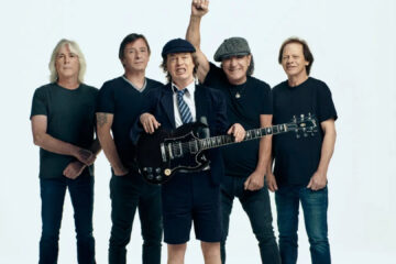 Integrantes do AC/DC posando para divulgação oficial com Angus Young ao centro, usando sua tradicional roupa escolar, segurando guitarra