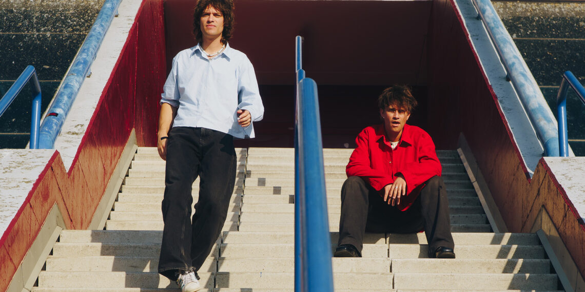 Integrantes da banda Balu Brigada posam em escadaria urbana em clima ensolarado, promovendo o single What Do We Ever Really Know?