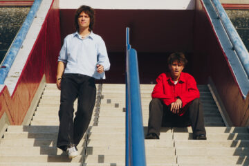 Integrantes da banda Balu Brigada posam em escadaria urbana em clima ensolarado, promovendo o single What Do We Ever Really Know?