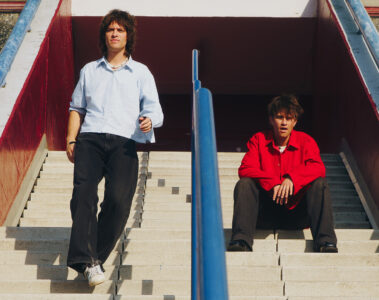 Integrantes da banda Balu Brigada posam em escadaria urbana em clima ensolarado, promovendo o single What Do We Ever Really Know?