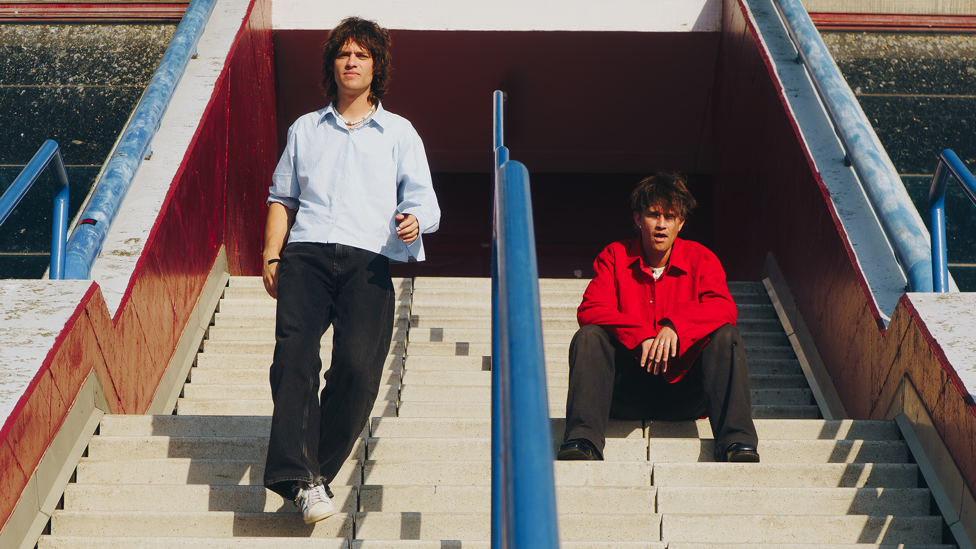 Integrantes da banda Balu Brigada posam em escadaria urbana em clima ensolarado, promovendo o single What Do We Ever Really Know?