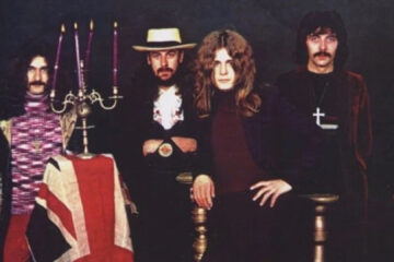 Foto clássica do Black Sabbath nos anos 1970, com Ozzy Osbourne, Tony Iommi, Geezer Butler e Bill Ward ao lado de um candelabro e bandeira britânica.