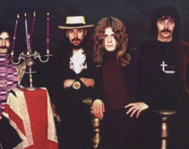 Foto clássica do Black Sabbath nos anos 1970, com Ozzy Osbourne, Tony Iommi, Geezer Butler e Bill Ward ao lado de um candelabro e bandeira britânica.