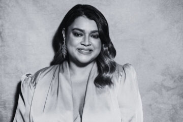 Preta Gil sorrindo em retrato em preto e branco com vestido claro e cabelo ondulado.