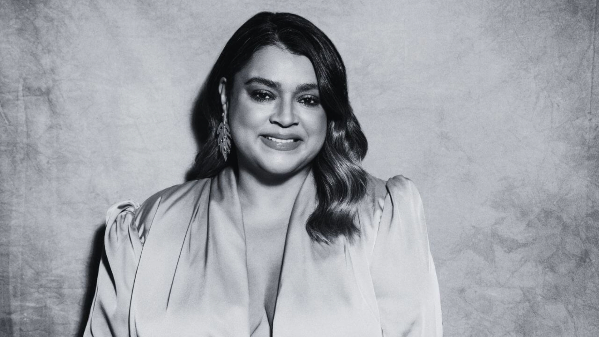 Preta Gil sorrindo em retrato em preto e branco com vestido claro e cabelo ondulado.