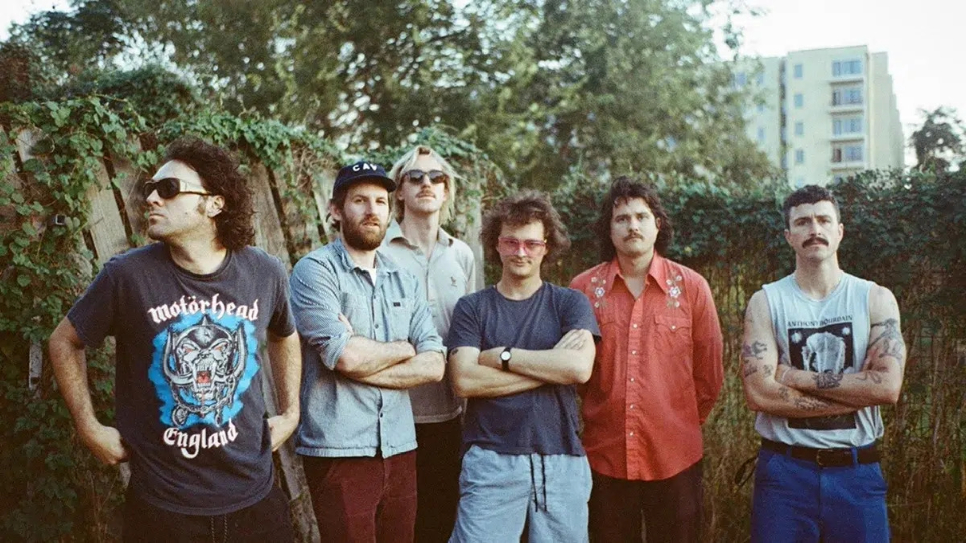 King Gizzard & The Lizard Wizard posa ao ar livre com os seis integrantes lado a lado, em clima descontraído.