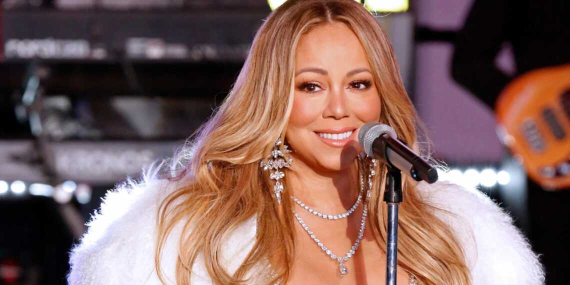 Mariah Carey sorrindo ao microfone durante apresentação, usando colar de diamantes