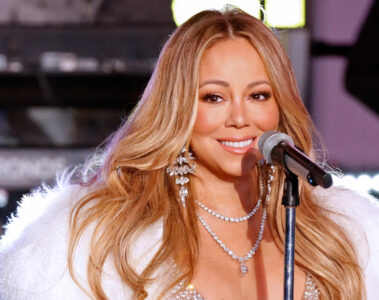 Mariah Carey sorrindo ao microfone durante apresentação, usando colar de diamantes