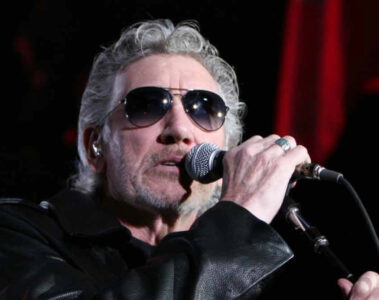Roger Waters cantando ao vivo com óculos escuros e jaqueta de couro