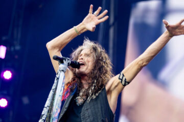 Steven Tyler com os braços erguidos durante sua participação no show "Back to the Beginning", em Birmingham