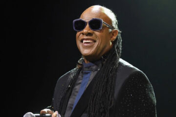 Stevie Wonder sorrindo no palco durante show ao vivo