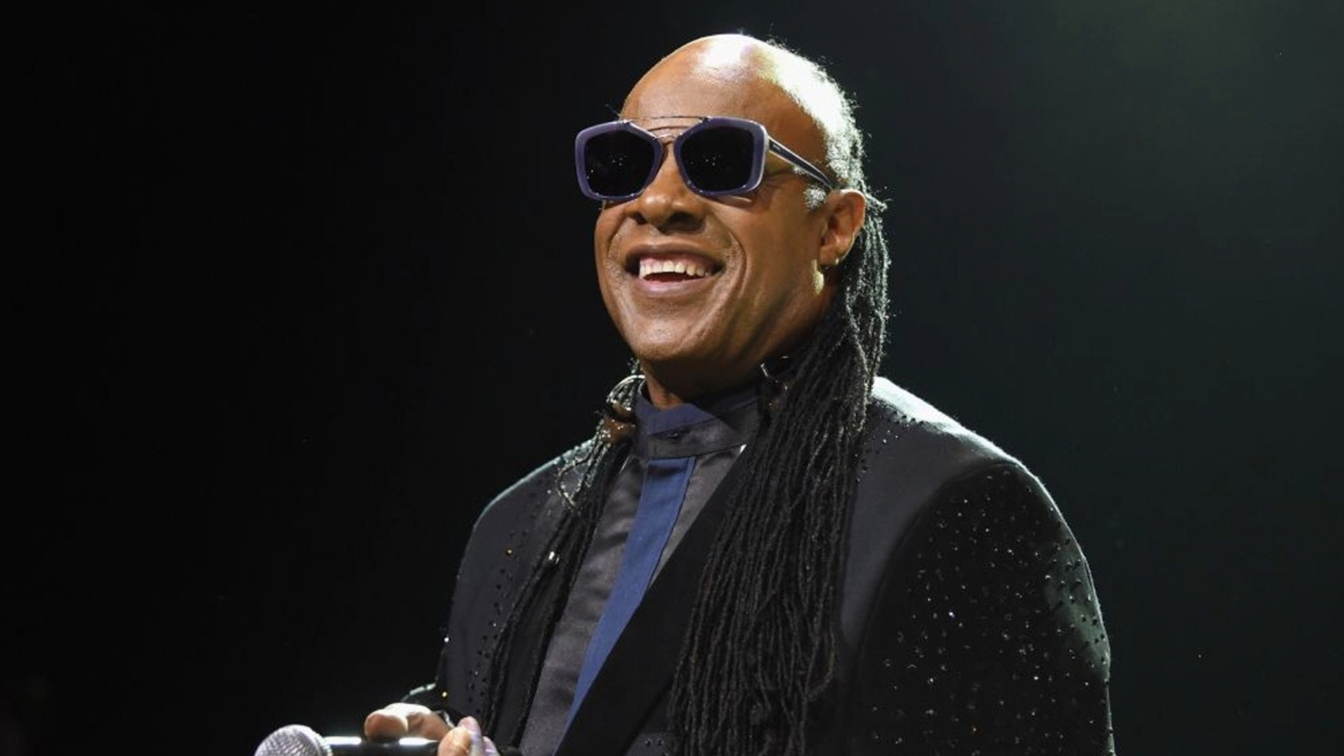 Stevie Wonder sorrindo no palco durante show ao vivo