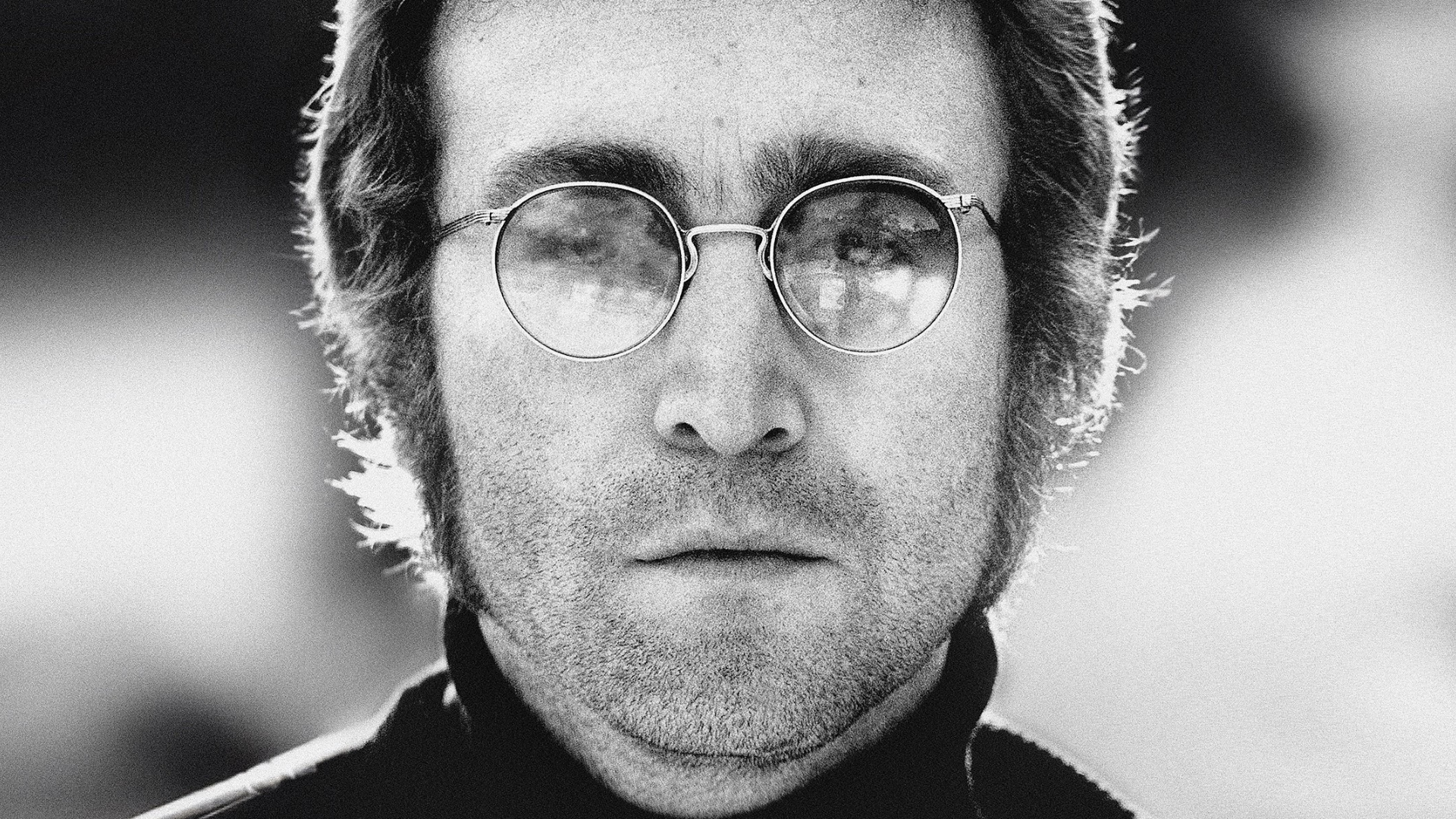 Retrato em preto e branco de John Lennon usando óculos redondos e expressão séria.