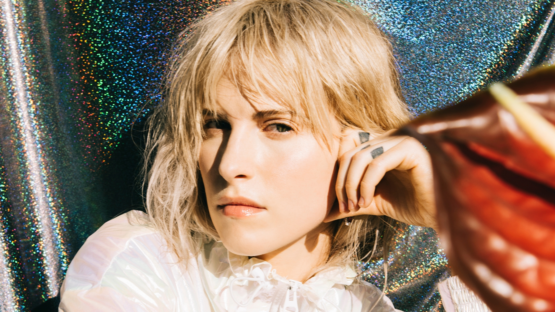 Hayley Williams em foto promocional com fundo brilhante, usando jaqueta branca e olhar intenso — crédito: Lindsey Byrnes
