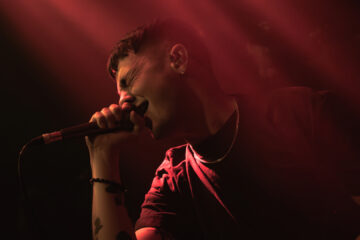 Henry Cox, vocalista do Boston Manor, cantando com intensidade durante show em São Paulo, sob luzes vermelhas dramáticas.