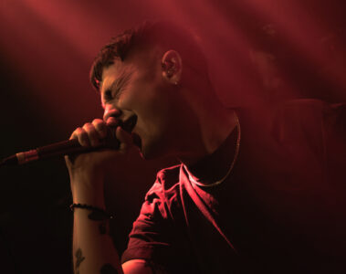 Henry Cox, vocalista do Boston Manor, cantando com intensidade durante show em São Paulo, sob luzes vermelhas dramáticas.