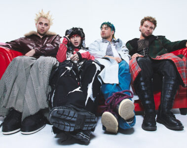 Banda 5 Seconds of Summer em ensaio promocional do álbum Everyone’s A Star! (2025), sentados em sofá vermelho com figurinos conceituais.