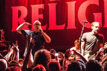 Bad Religion se apresenta ao vivo em show de punk rock, com vocalista e baixista à frente do palco diante do público.