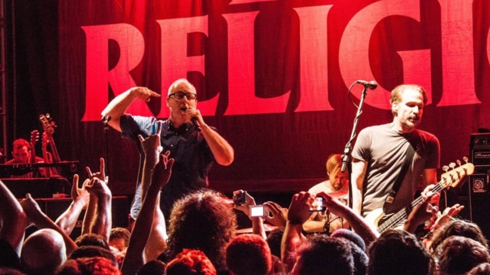 Bad Religion se apresenta ao vivo em show de punk rock, com vocalista e baixista à frente do palco diante do público.