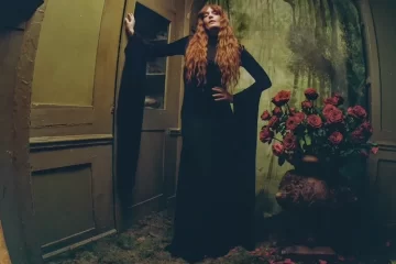 Florence Welch posa em um cenário sombrio ao lado de um vaso de rosas vermelhas para divulgar o novo single One of the Greats e o álbum Everybody Scream.