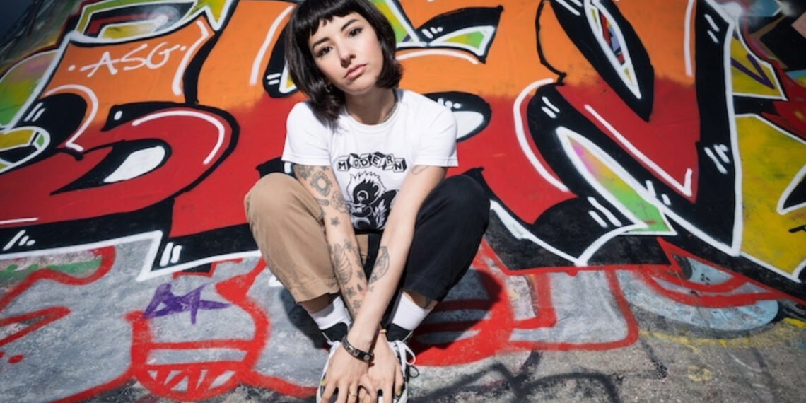 Karen Dió posa em frente a um grafite colorido, reforçando a atitude punk de seu novo single "Cut Your Hair".