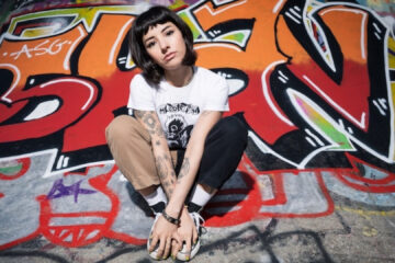 Karen Dió posa em frente a um grafite colorido, reforçando a atitude punk de seu novo single "Cut Your Hair".