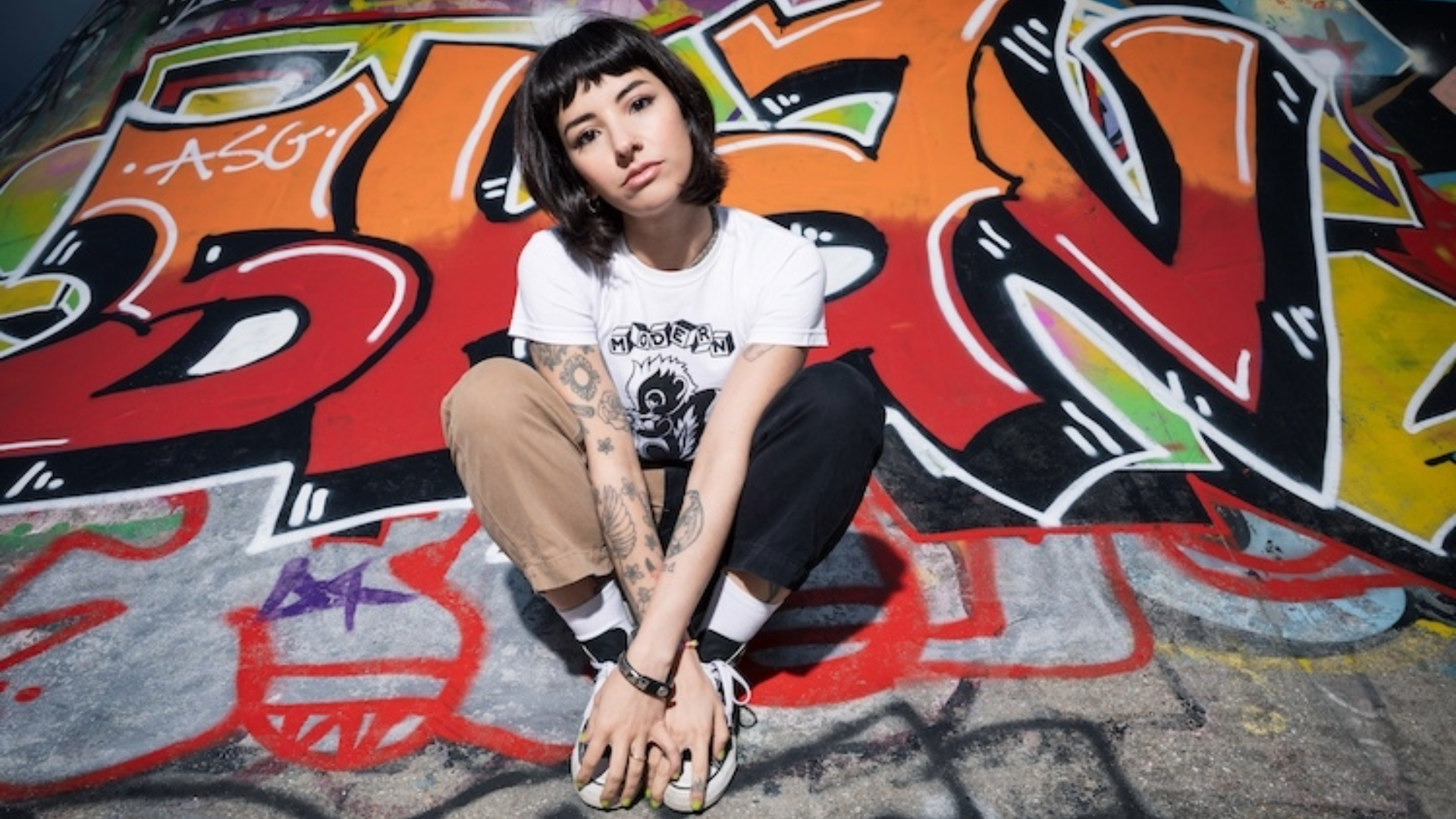 Karen Dió posa em frente a um grafite colorido, reforçando a atitude punk de seu novo single "Cut Your Hair".