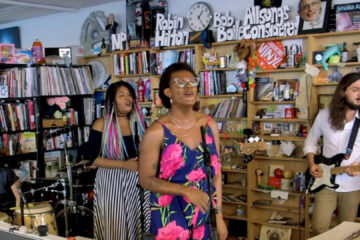 Liniker se apresenta no Tiny Desk, acompanhada por sua banda, em performance intimista com estantes de livros ao fundo.
