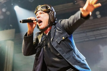 Bruce Dickinson, vocalista do Iron Maiden, cantando ao vivo em show solo, usando figurino de aviador e segurando o microfone.