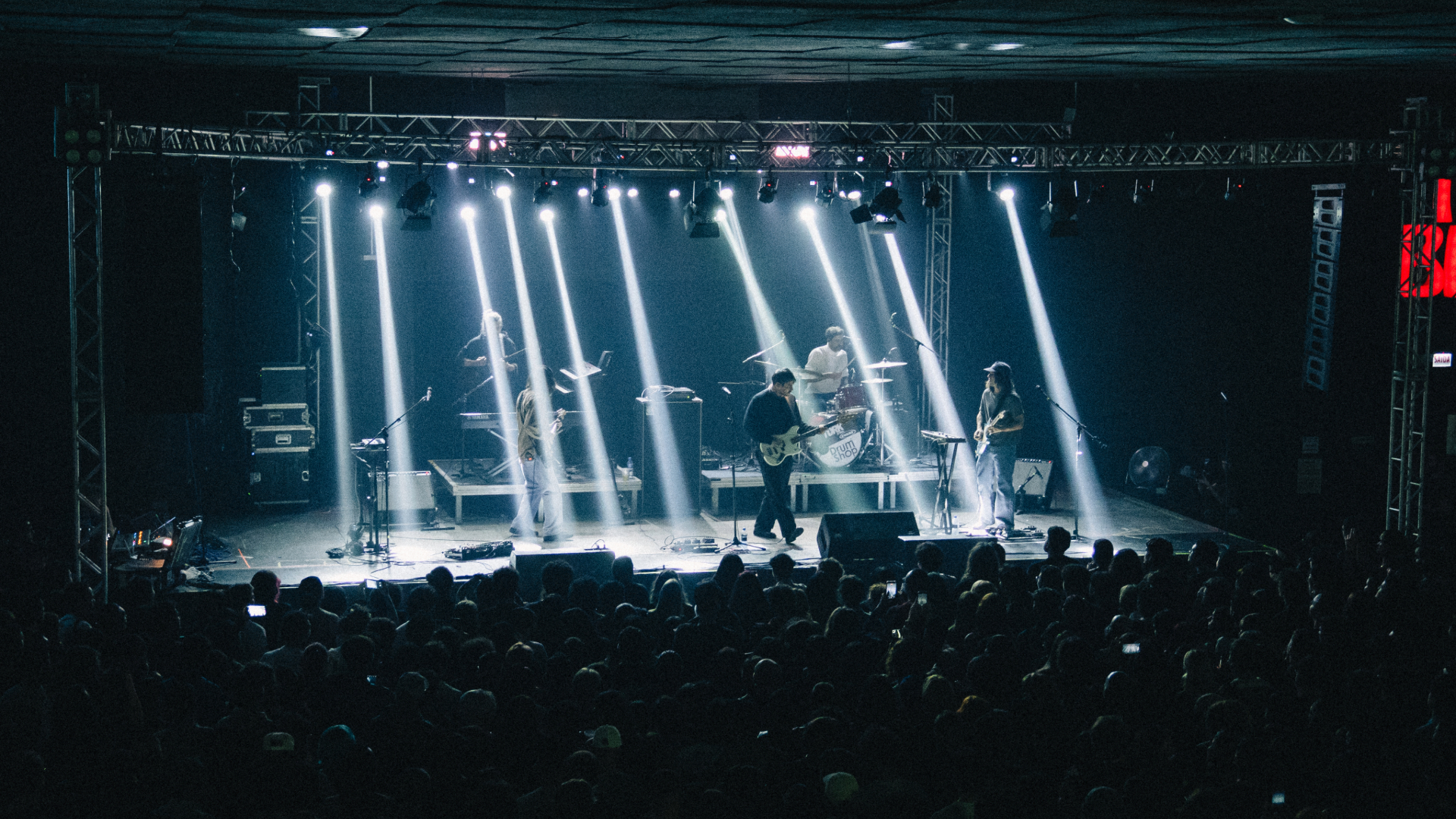 Terno Rei se apresentando no Tork n’ Roll em Curitiba com luzes verticais iluminando o palco e plateia lotada
