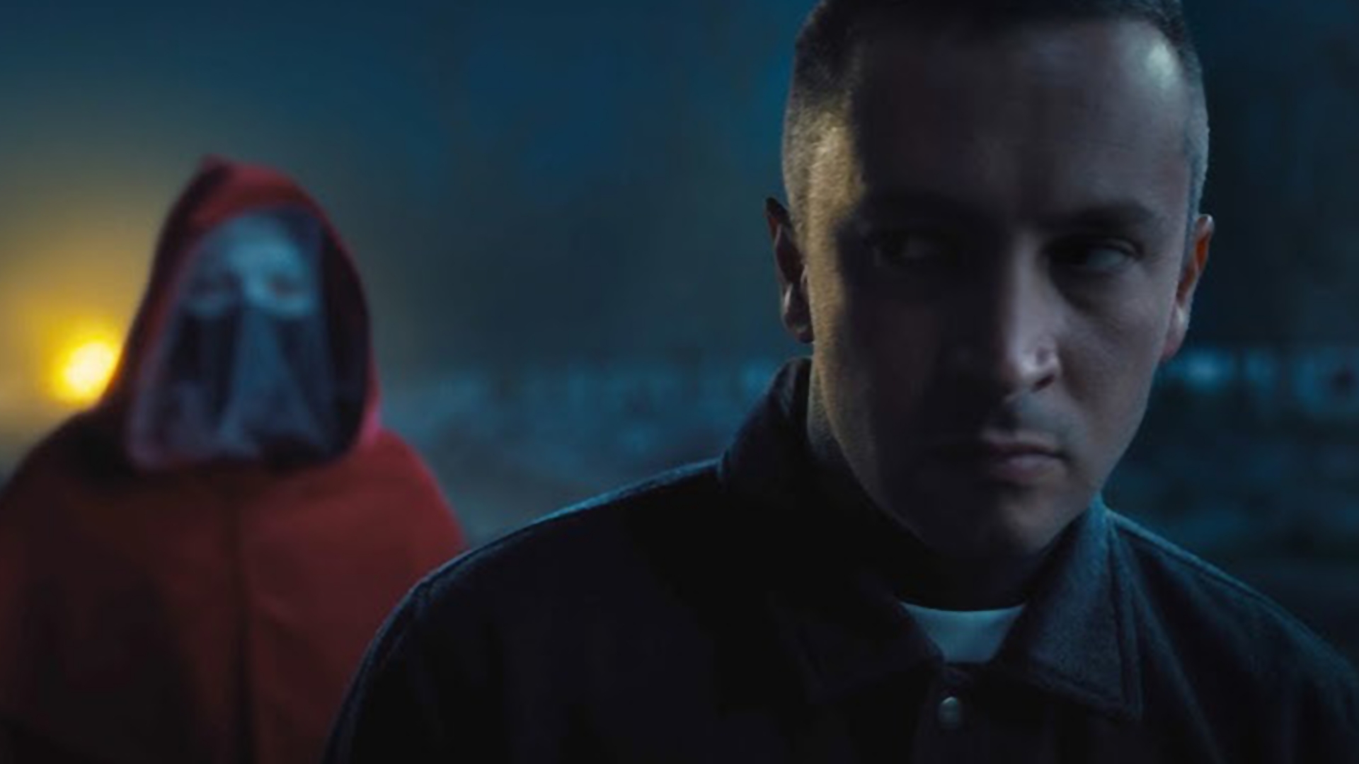 Cena do videoclipe City Walls do Twenty One Pilots, com Tyler Joseph em destaque e uma figura encapuzada ao fundo.