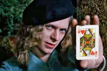 David Bowie jovem em foto de Keith MacMillan, segurando a carta da Rainha de Copas, em retrato criativo e icônico.