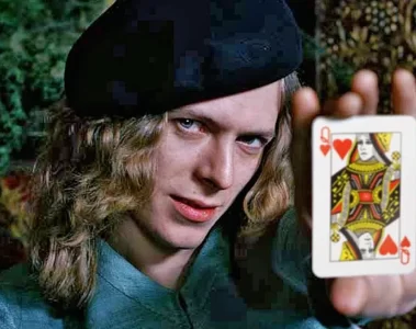 David Bowie jovem em foto de Keith MacMillan, segurando a carta da Rainha de Copas, em retrato criativo e icônico.