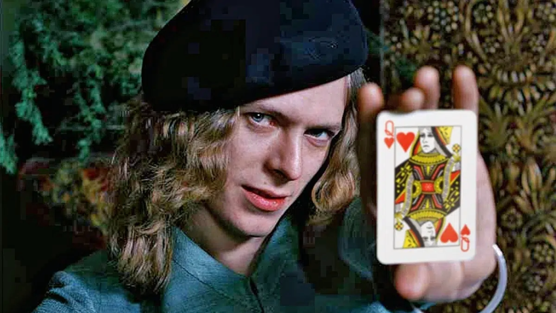 David Bowie jovem em foto de Keith MacMillan, segurando a carta da Rainha de Copas, em retrato criativo e icônico.
